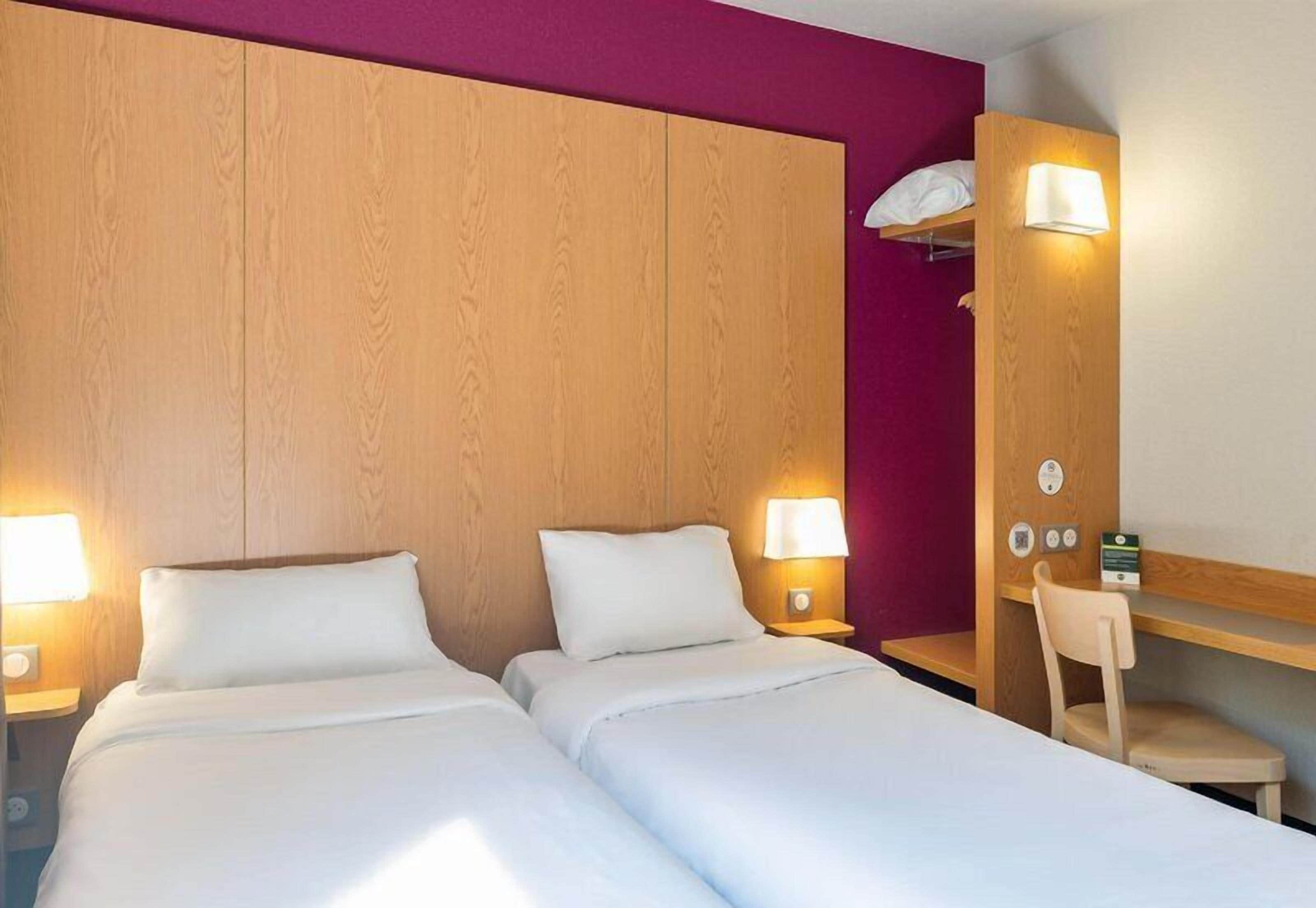 Ein Hotelzimmer mit zwei Betten, einem Schreibtisch, einem Sessel und einem Holzkopfstück.