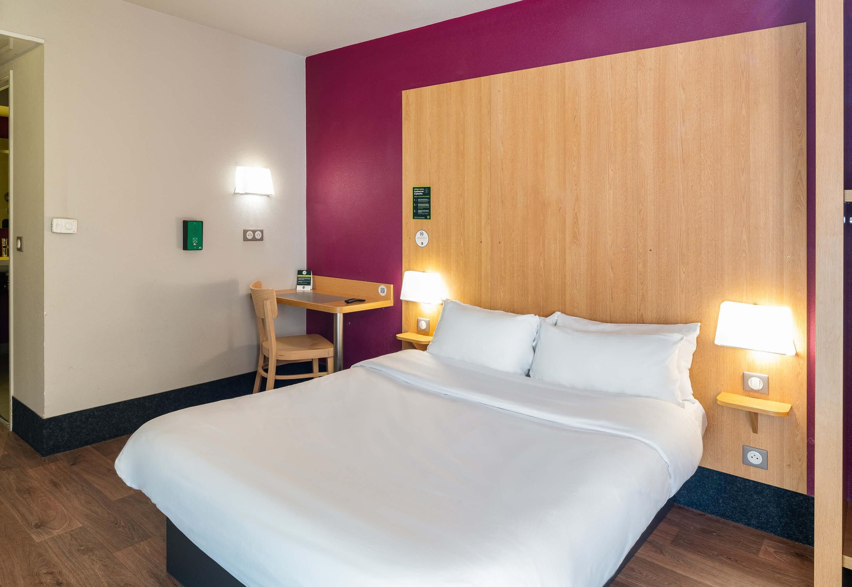 Ein Hotelzimmer mit einem großen Bett, einem Schreibtisch, zwei Nachttischlampen und einem Holzkopfteil.