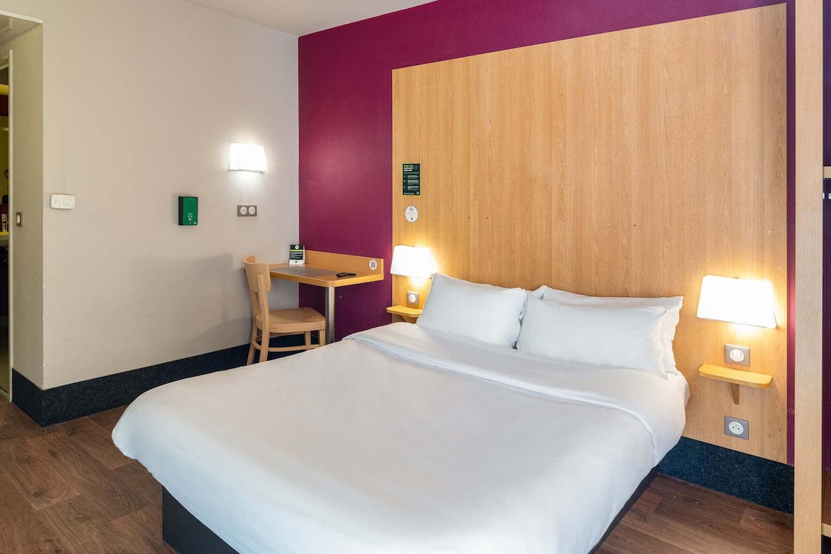 A hotel room with a large bed, a desk, two bedside lamps, and a wooden headboard.