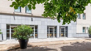 A modern building with a paved entrance, large windows, and a potted plant in the foreground. - B&B HOTEL Lyon Caluire Cité Internationale (Caluire-et-Cuire)