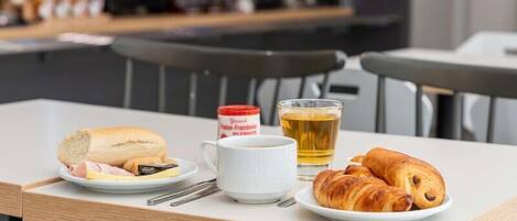 A table with croissants, a plate with ham and cheese, a cup of coffee, and a glass of tea.