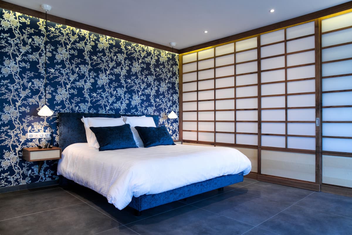 Une chambre moderne avec un grand lit, une literie bleu foncé et un paravent japonais traditionnel en papier.