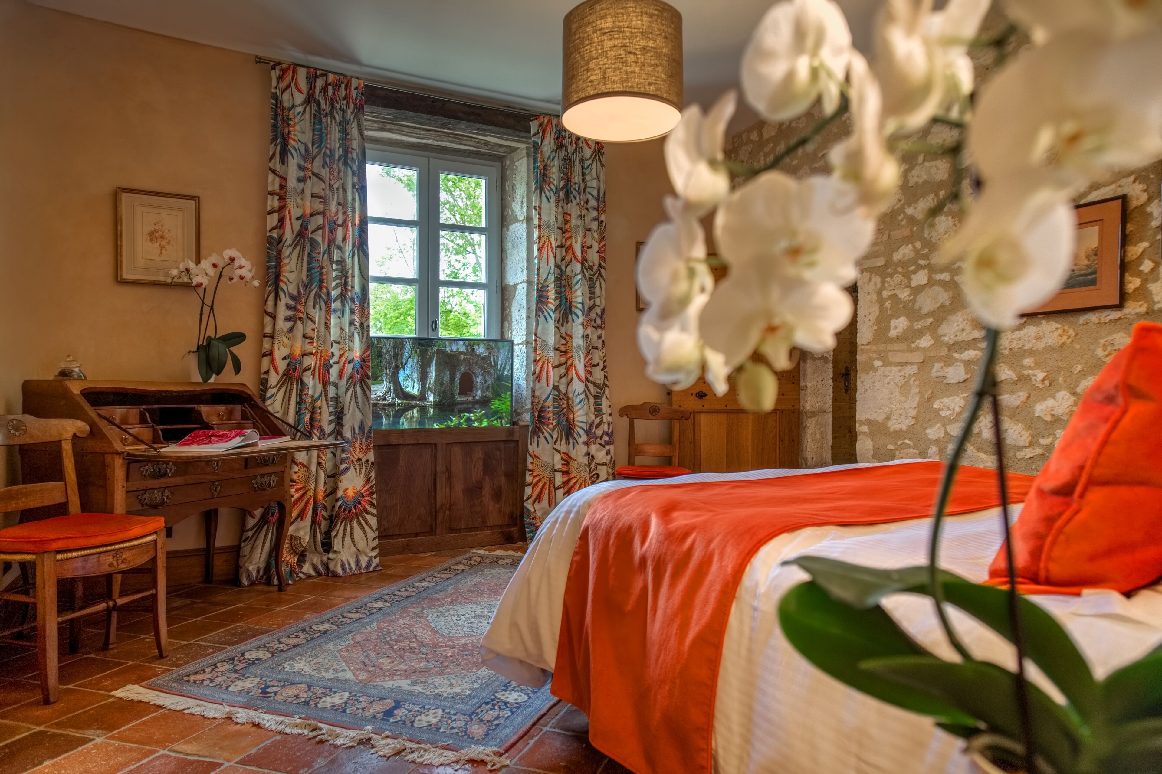 Un dormitorio con cama, escritorio, silla, ventana con cortinas y una lámpara colgante.