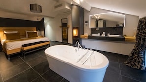 Une chambre moderne dotée d’un grand lit, d’un coin salon séparé, d’une baignoire et d’une salle de bain avec un grand miroir et un meuble-lavabo.
