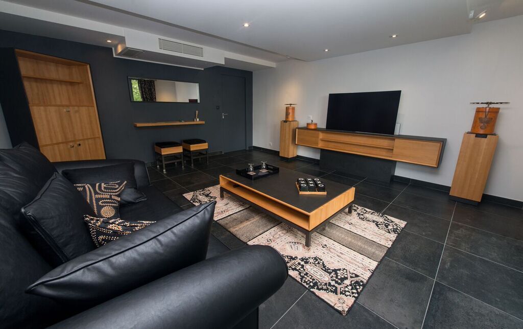 Un salon moderne avec un canapé en cuir noir, une table basse en bois, un téléviseur à écran plat fixé au mur et un meuble en bois.