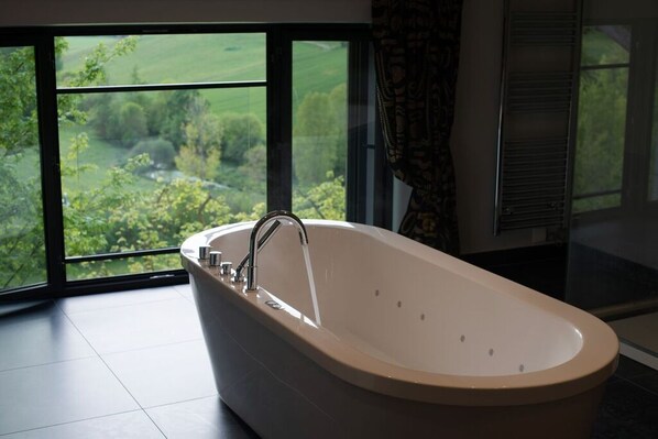 Un baño moderno con una bañera independiente, amplias ventanas que ofrecen vistas a zonas verdes y un perchero para toallas.