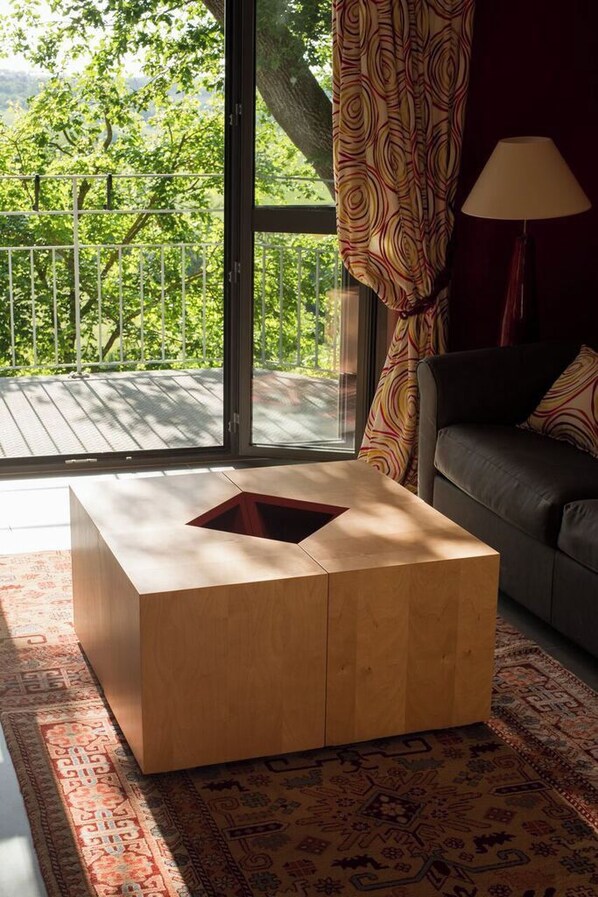 A room with a large window, a sofa, a patterned rug, and a wooden coffee table. - Domaine de Nazère (Avezan)