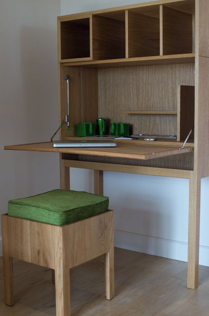 A wooden desk with a green cushioned stool, a laptop, and a green mug.