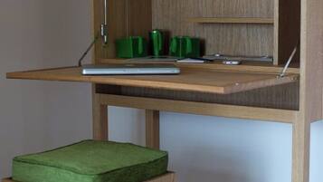 A wooden desk with a green cushioned stool, a laptop, and a green mug.