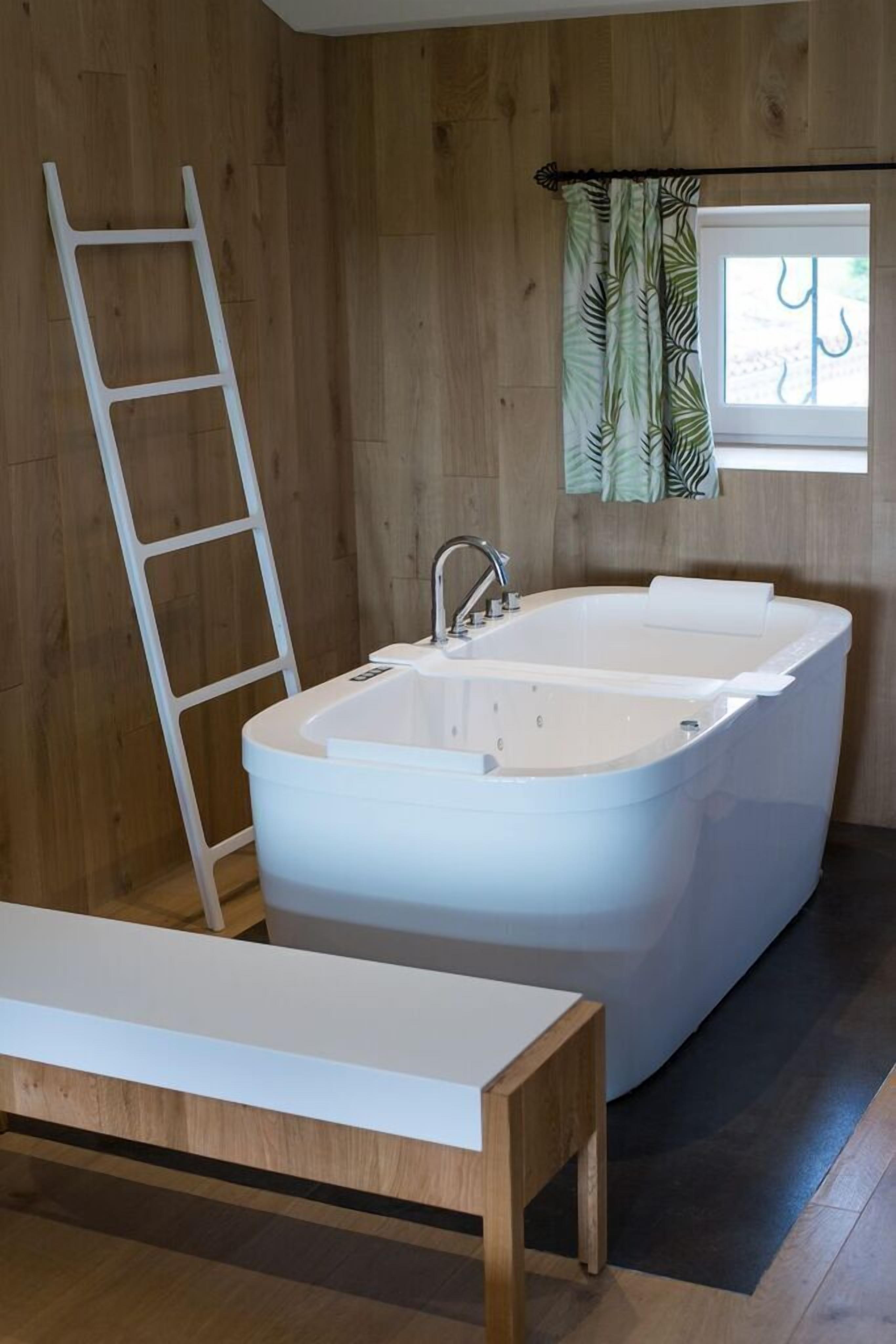 Une salle de bain moderne avec une baignoire sur pieds, un banc en bois et une fenêtre avec des rideaux.