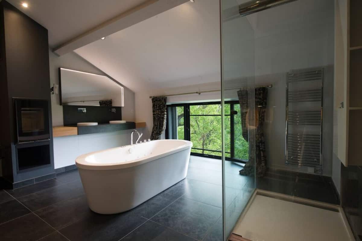 Une salle de bain moderne avec une baignoire sur pieds, une douche à parois de verre et une grande fenêtre donnant sur un paysage verdoyant.