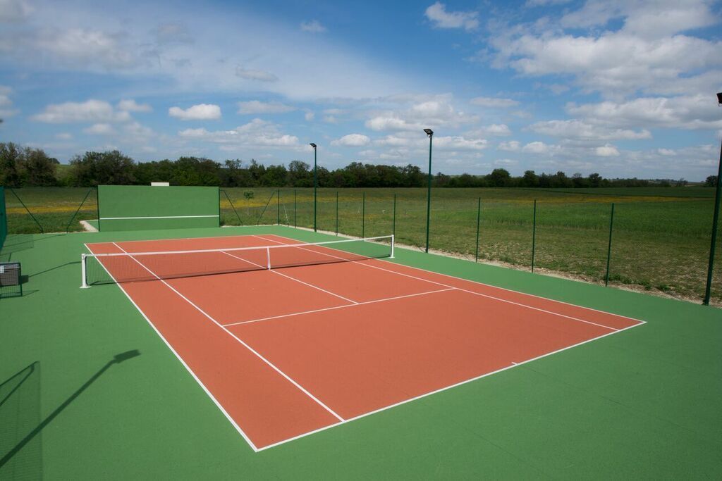 A tennis court with a green and red surface, surrounded by a fence and trees.
