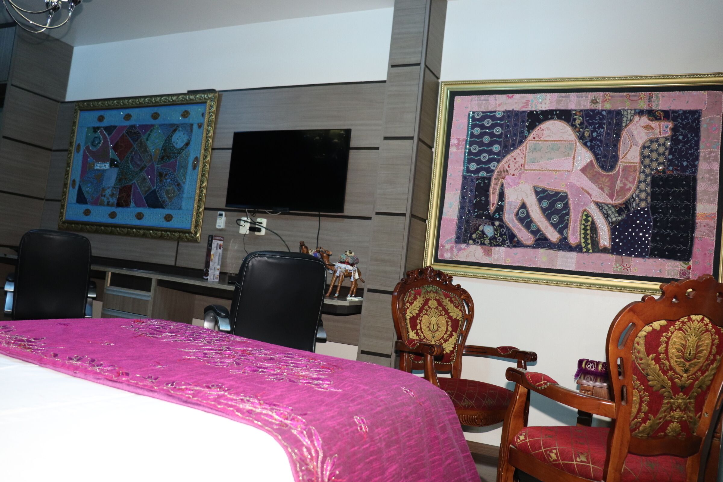 Une chambre d’hôtel comprenant un lit, deux chaises, un bureau, un téléviseur à écran plat et deux œuvres d’art encadrées accrochées au mur.