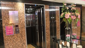 An elevator interior with a digital display, a marble wall, and a reception desk with a vase of flowers. - Hotel Luxsur (Encarnacion)