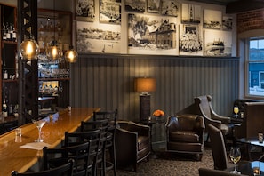 A bar area with a wooden counter, multiple bar stools, and a wall adorned with black and white photographs.