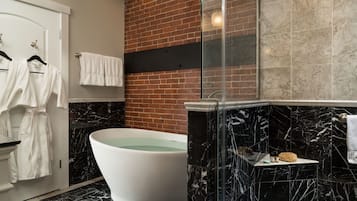 Une salle de bain moderne avec une baignoire sur pieds, une douche à parois de verre et un mur d’accent en briques.