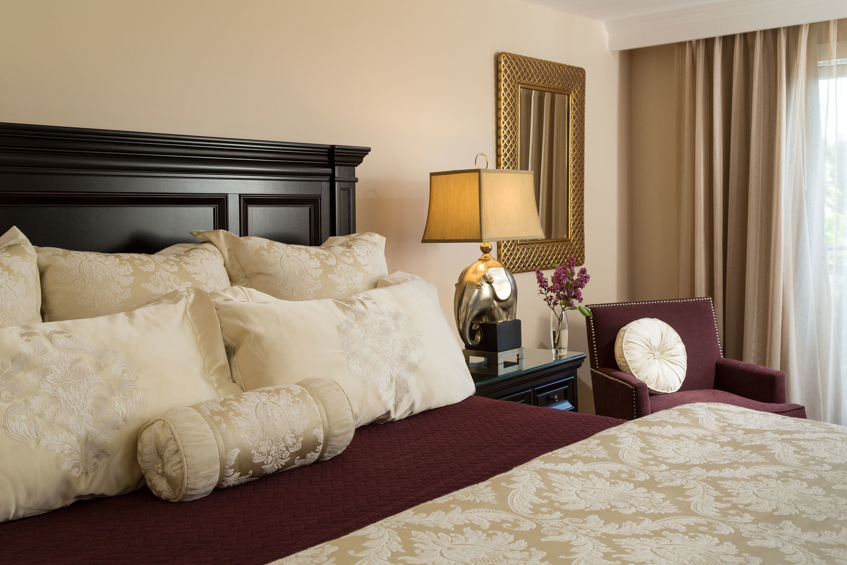 A hotel room with a large bed, a nightstand with a lamp, a chair, and a mirror on the wall.