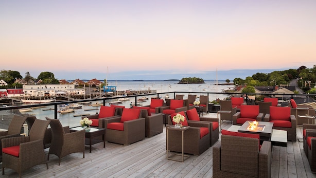 A deck with wicker furniture and red cushions, overlooking a marina with boats and a distant island. - 16 Bay View (Camden)