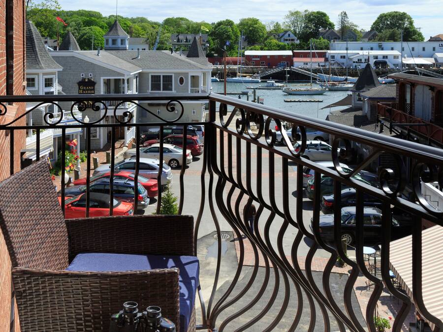A balcony with wicker furniture overlooking a marina with boats and a parking area.