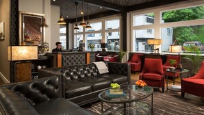 A modern hotel lobby with a black leather sofa, red armchairs, and a glass coffee table. - 16 Bay View (Camden)