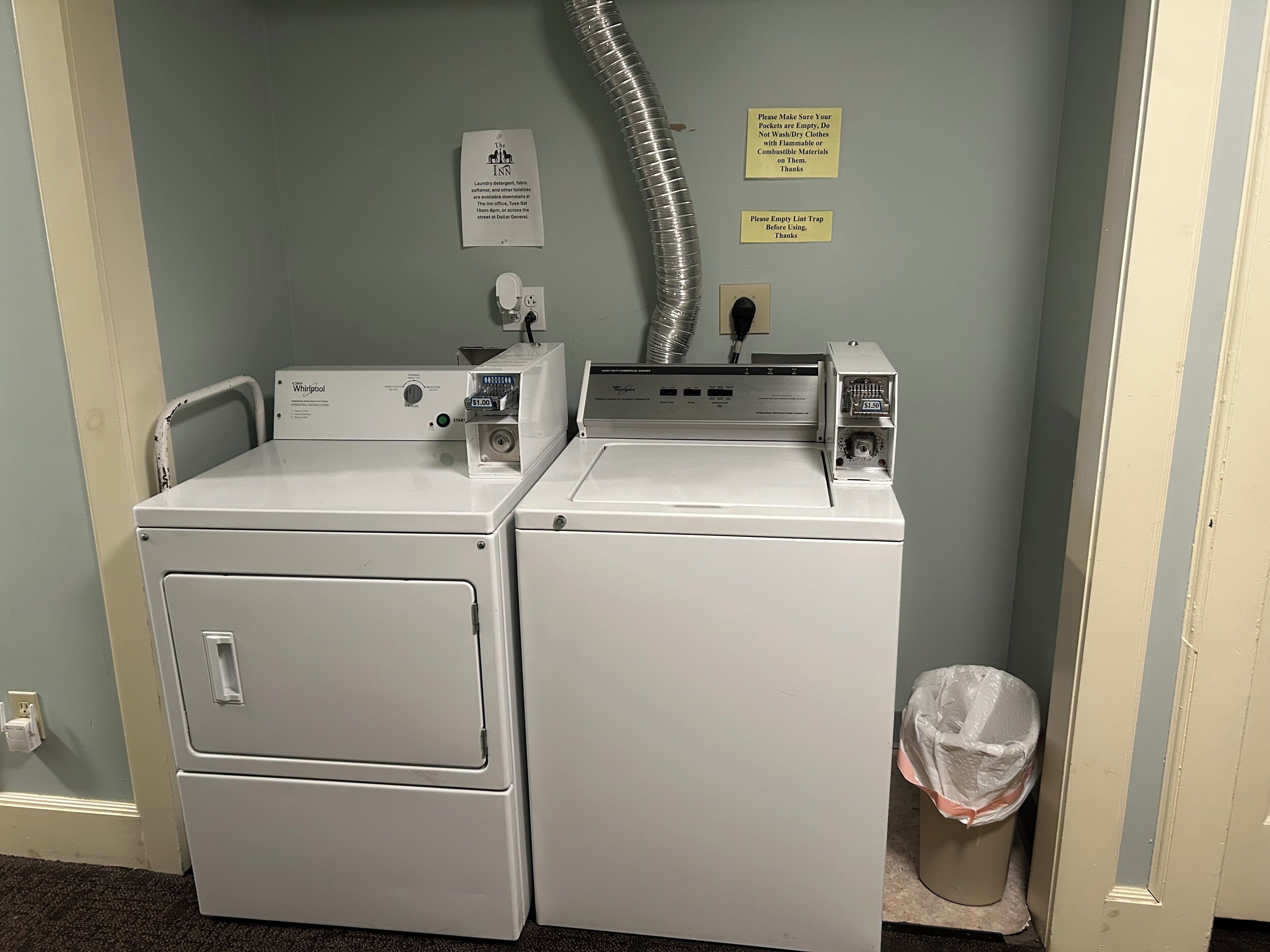 A laundry area with two Whirlpool washers, a lint trap, and two signs on the wall.