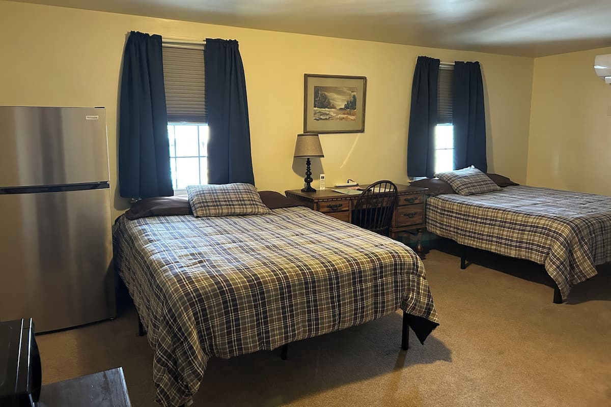 A room with two beds, a desk, a lamp, a chair, and a refrigerator.