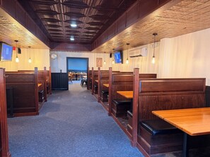Interior de restaurante con cabinas y mesas, techo de madera y televisores en la pared.