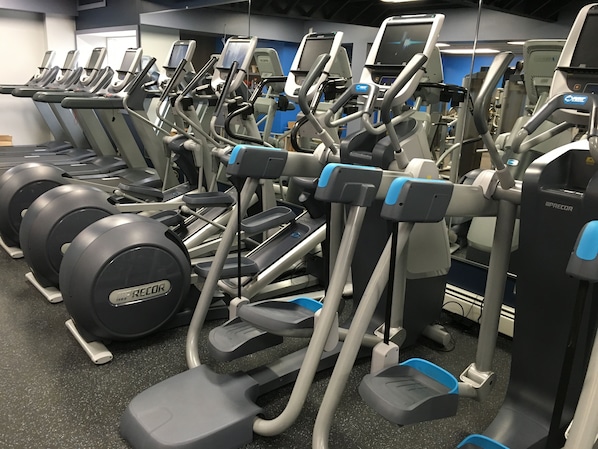 Une rangée de tapis de course et d’appareils de musculation elliptique dans une salle de sport.
