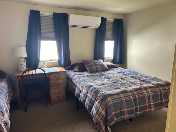 A bedroom with a bed, a desk, a chair, and an air conditioning unit.