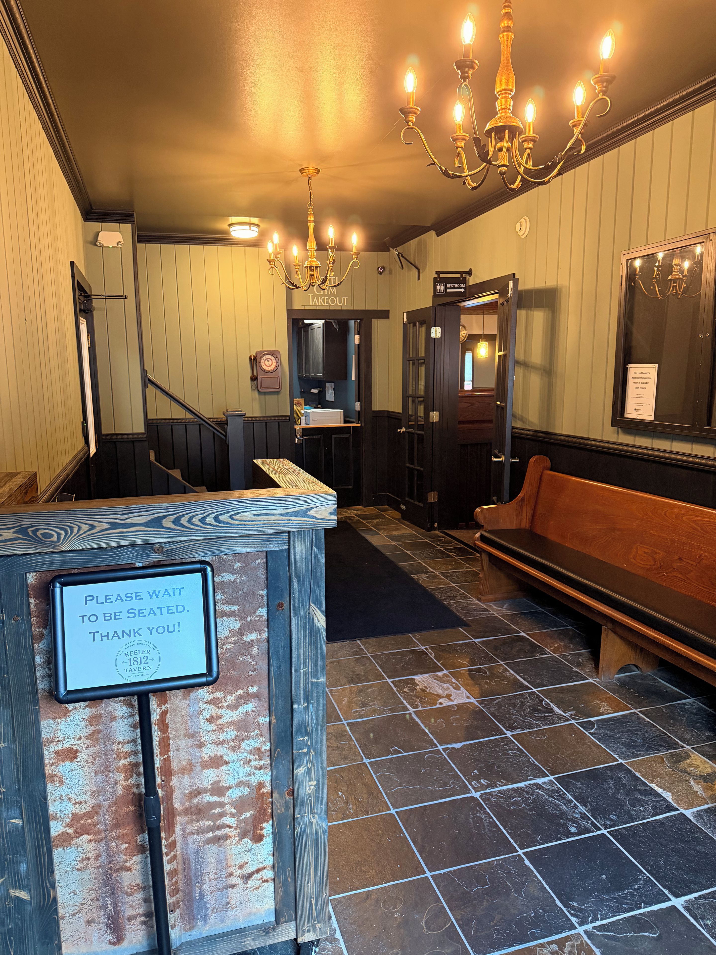 A hotel lobby with a wooden bench, a sign indicating a restroom, and a chandelier.