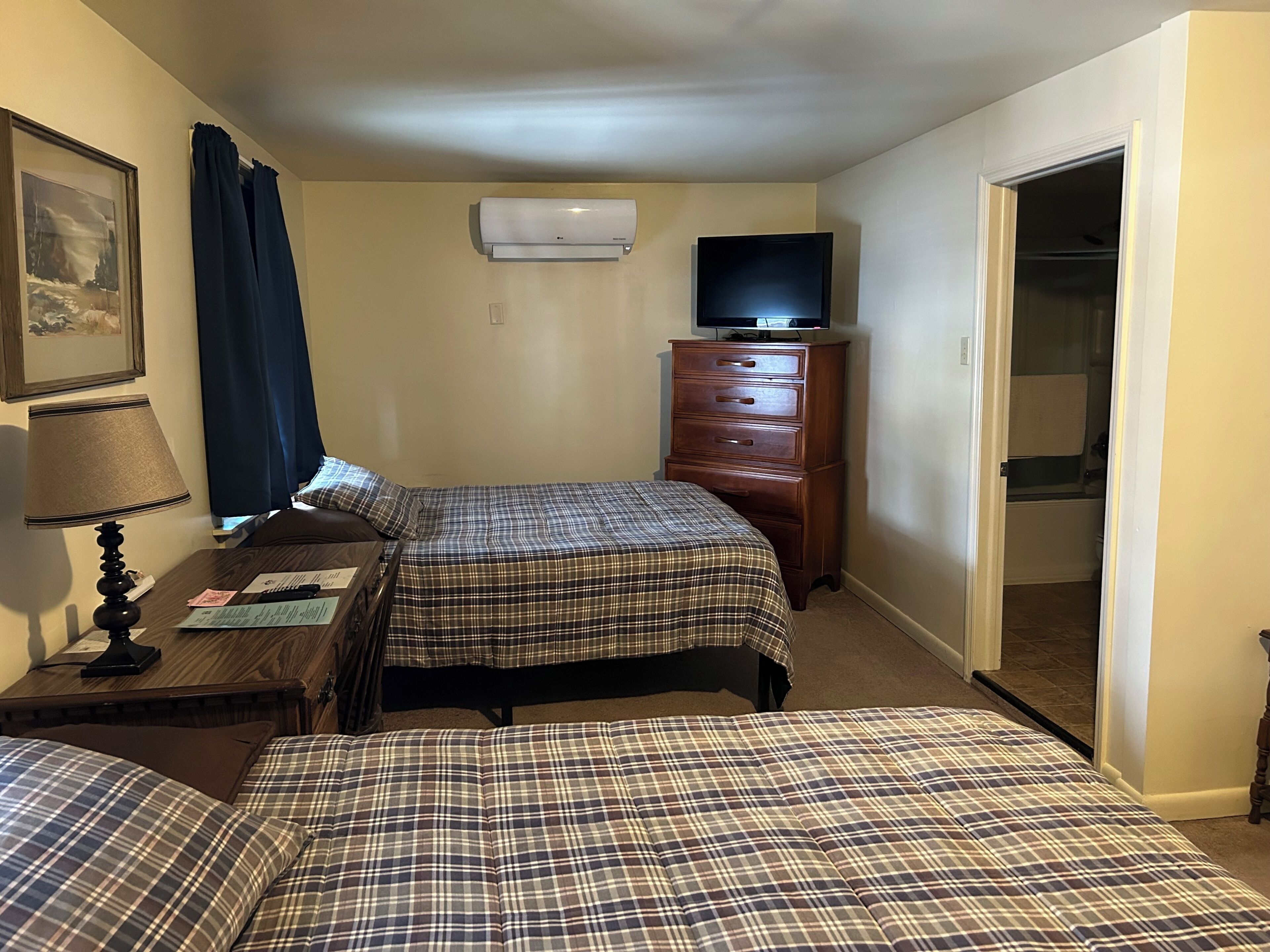 Habitación de hotel con dos camas, tocador, televisor y aire acondicionado.
