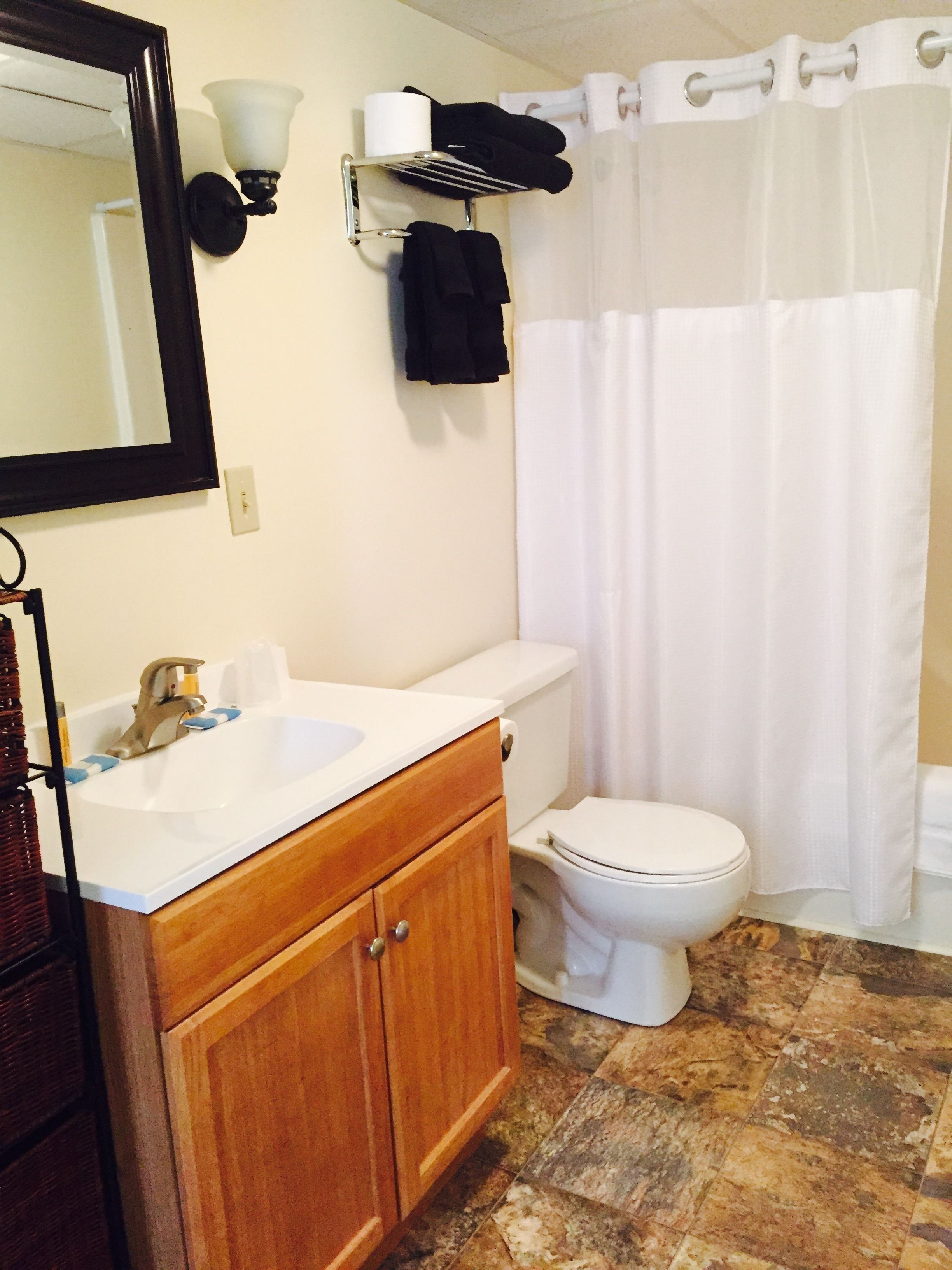 Un baño con un lavabo blanco, tocador de madera, inodoro, cortina de ducha y un perchero de toallas en la pared.