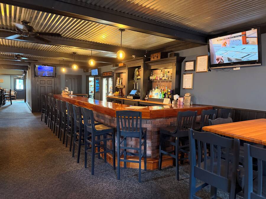 Zona de bar con una barra alargada, diversas opciones de asiento y un televisor en la pared.