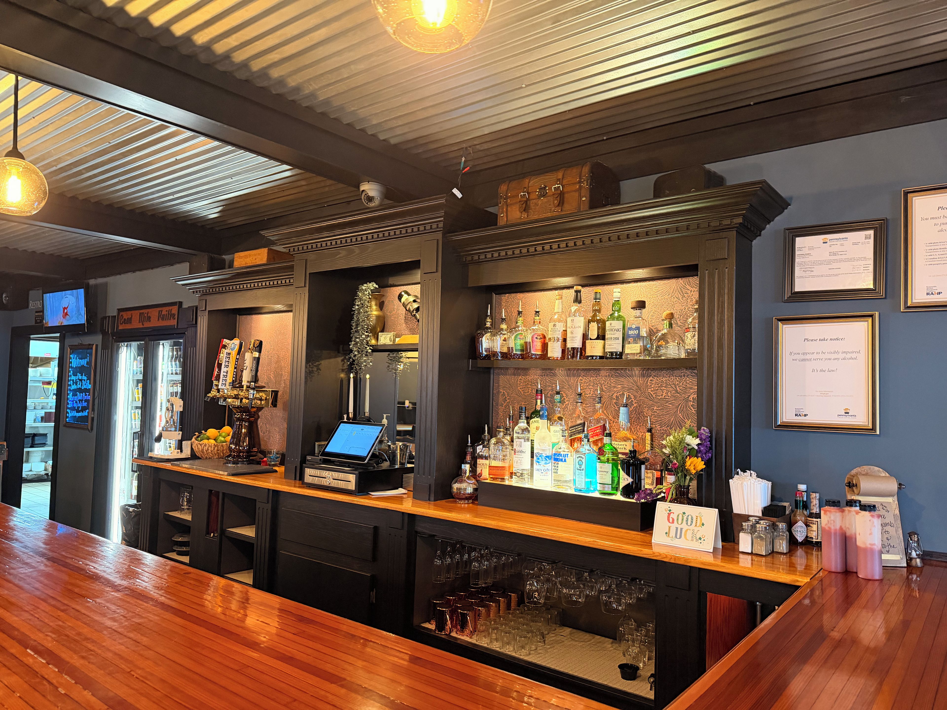 A bar area with a wooden counter, shelves of liquor bottles, and a cash register.