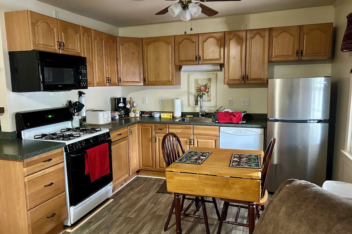 A kitchen with wooden cabinets, a stove, microwave, refrigerator, and a dining table with chairs.