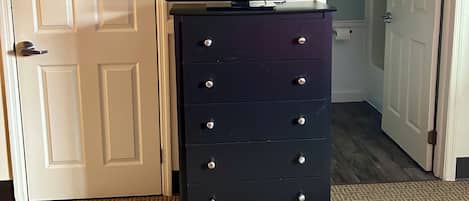 A room with a flat-screen TV on a black dresser, white doors, and a carpeted floor.