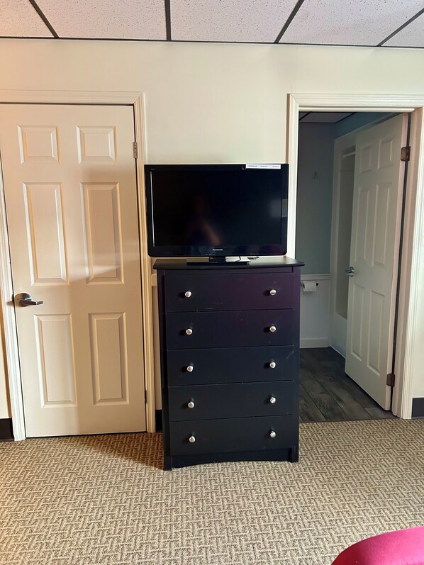 A room with a flat-screen TV on a black dresser, white doors, and a carpeted floor. - The Montrose Hotel (Montrose)
