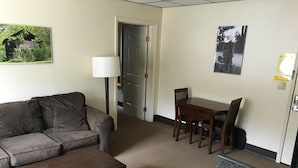 A living room with a sofa, a coffee table, a dining table with chairs, a lamp, and a door leading to another room. - The Montrose Hotel (Montrose)