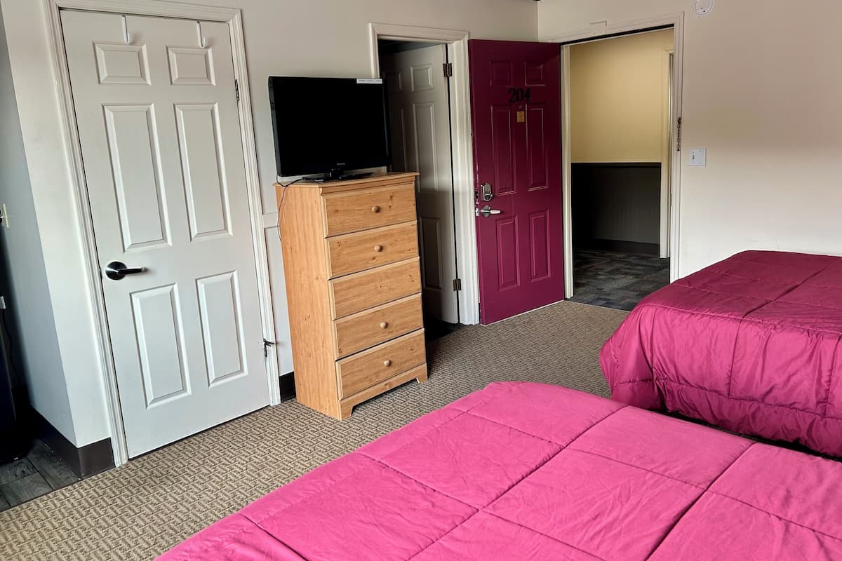 A hotel room with a bed, a dresser, a television on top, and a door with the number 204.