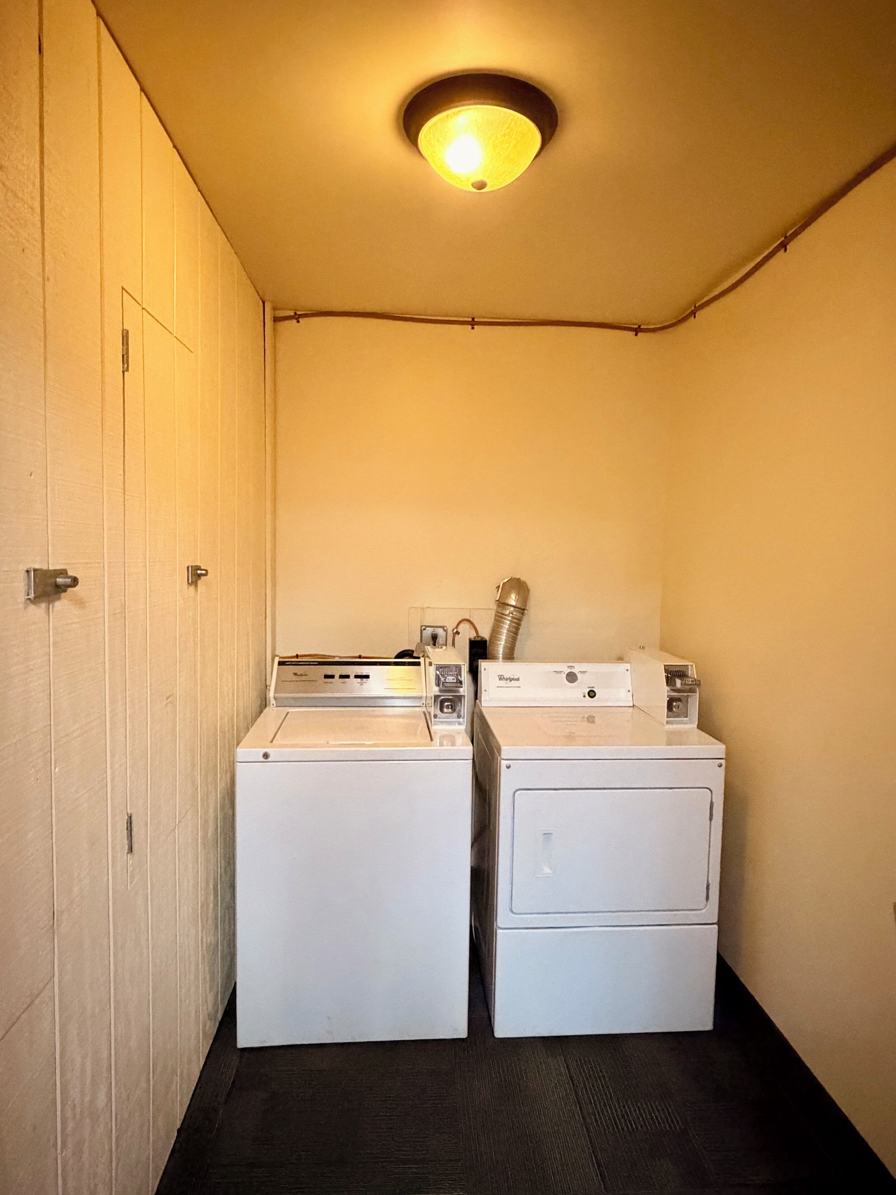 A laundry room with two white washers and dryers, wooden walls, and a ceiling light.