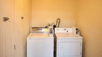 A laundry room with two white washers and dryers, wooden walls, and a ceiling light.