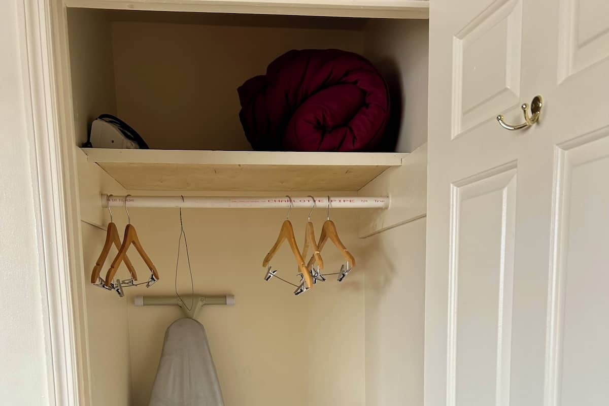 A small storage closet with a mattress, a metal shelf, and a wooden door.