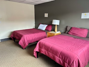 Una camera d'albergo con due letti, ciascuno con copripiumino rosa, un comodino con una lampada e una sveglia a muro.