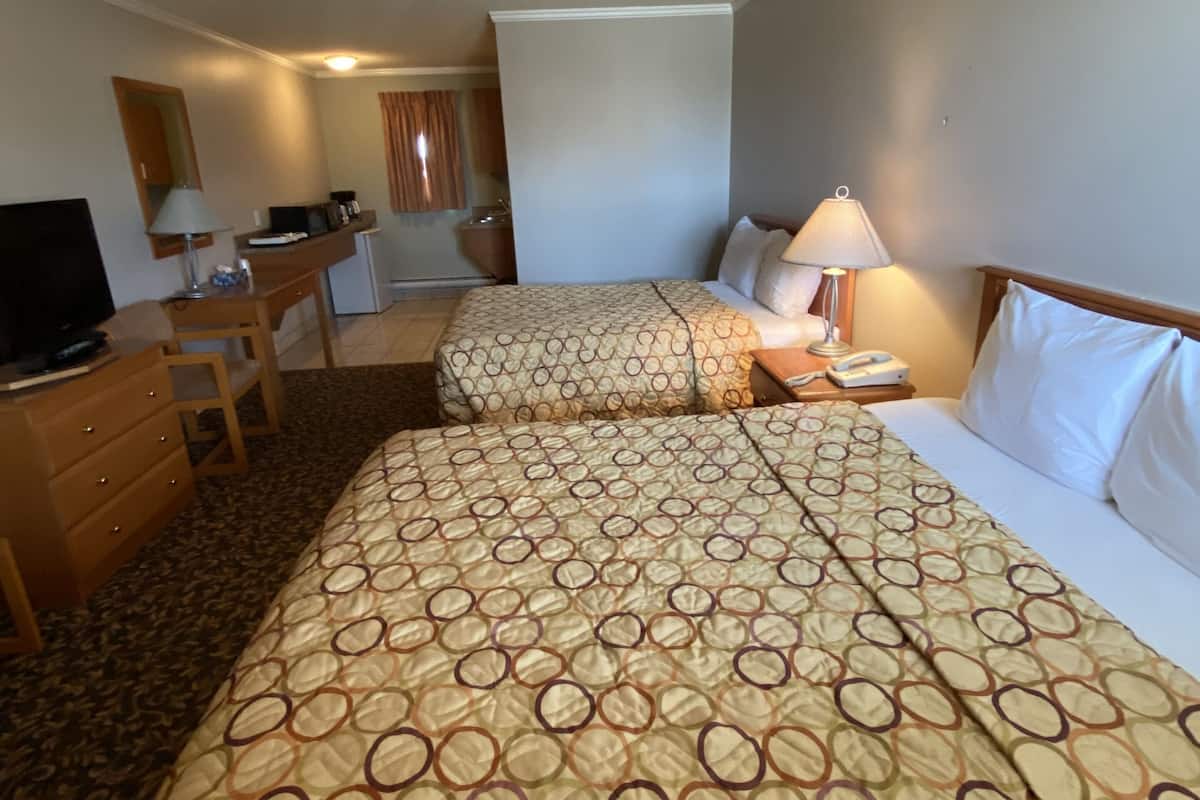 A hotel room with two beds, a desk, a television, and a bathroom visible through an open door.