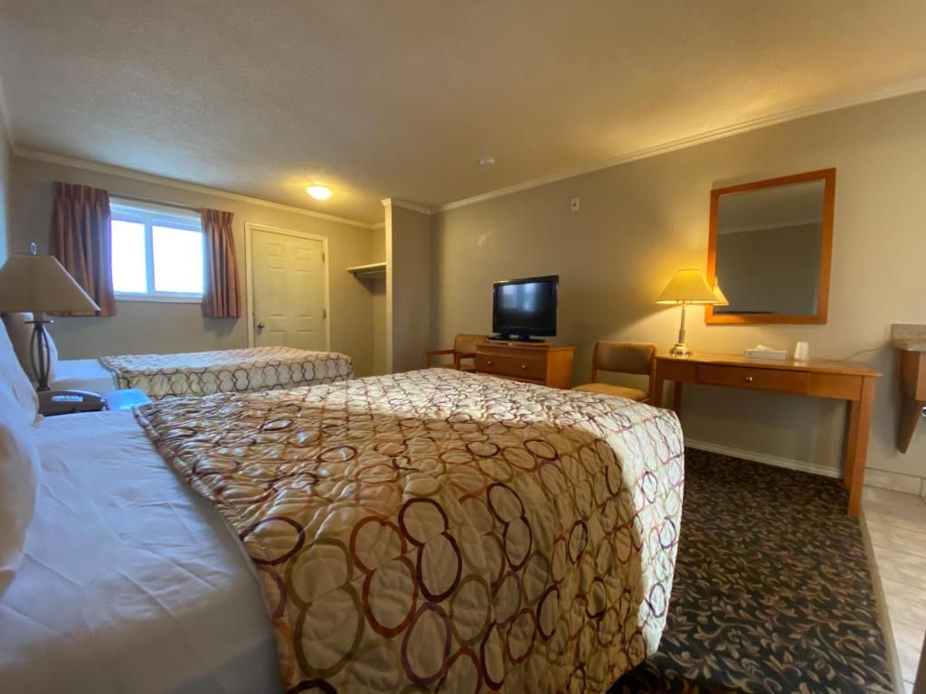 Habitación de hotel con dos camas, televisión, escritorio con lámpara y espejo en la pared.