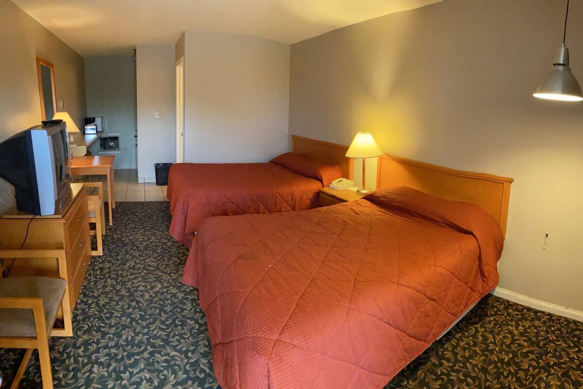 A hotel room with two beds, a desk with a computer, and a small seating area.