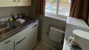 A compact kitchen with a sink, stove, and a window with curtains. - Aspen Motor Inn (Drayton Valley)