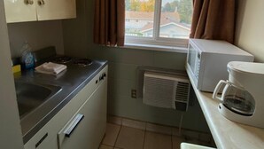 A compact kitchen with a stove, microwave, and coffee maker. There is a window with curtains, and a view of houses outside. - Aspen Motor Inn (Drayton Valley)