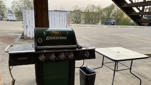 A portable Eskimos grill with four burners, a side table, and a trash bin. - Aspen Motor Inn (Drayton Valley)