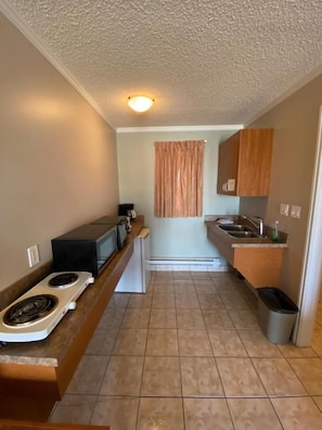 A compact kitchen with a stove, microwave, and sink. - Aspen Motor Inn (Drayton Valley)